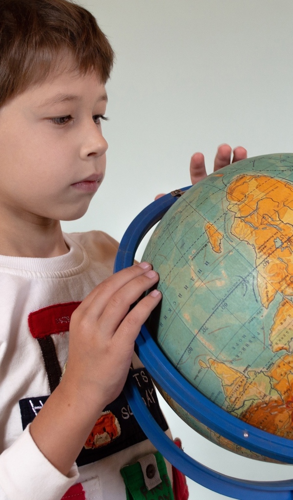 Школьник изучает глобус на сером фоне