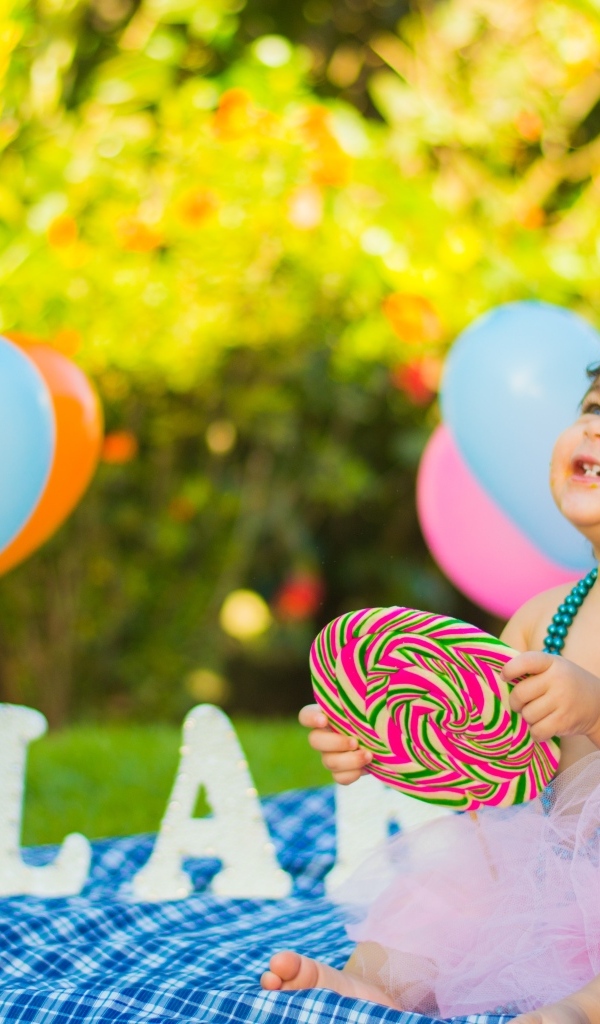 Улыбающаяся маленькая девочка с большой конфетой