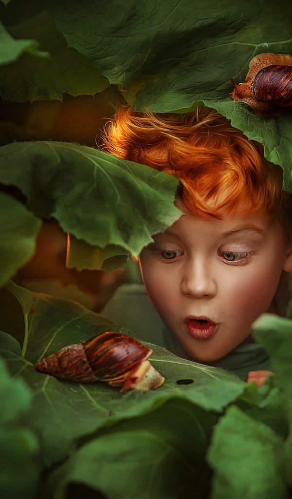 Удивленный рыжеволосый мальчик смотрит на улитку
