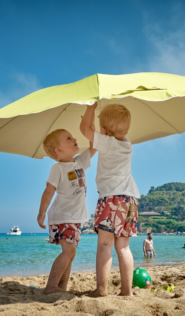 Два мальчика на пляже под зонтом
