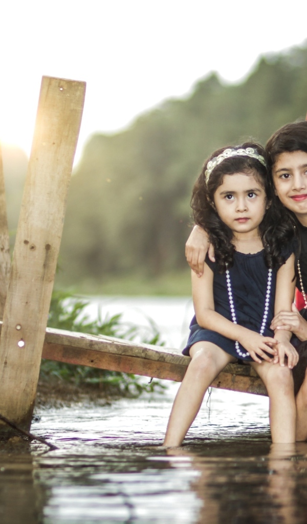 Две девочки сидят на мосту у реки
