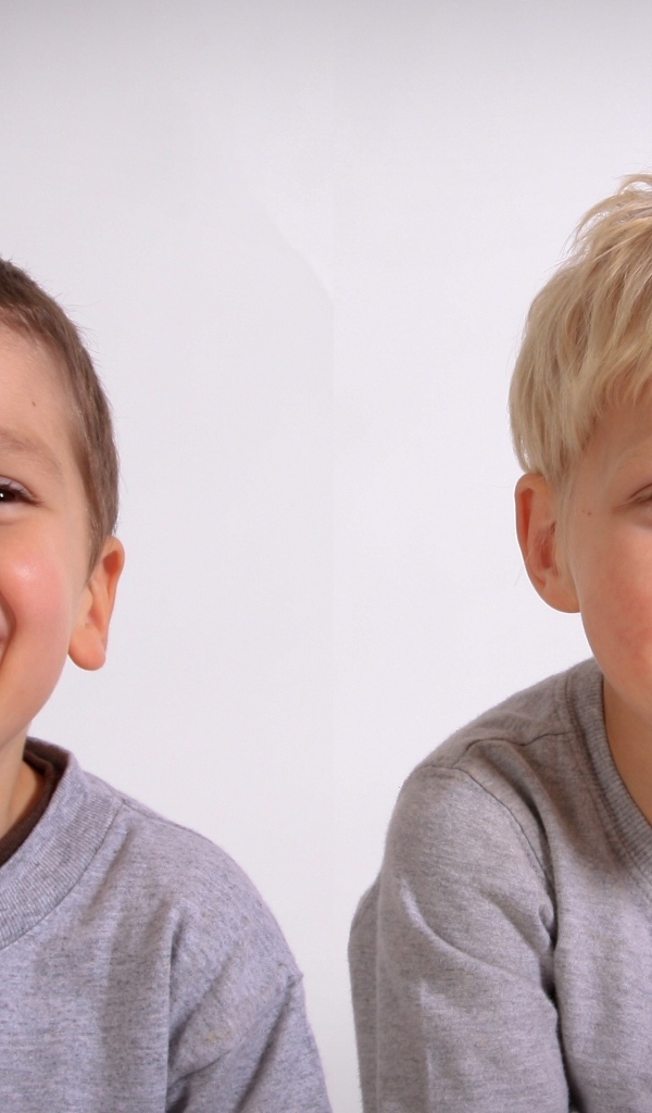 Два смеющихся маленьких мальчика на сером фоне