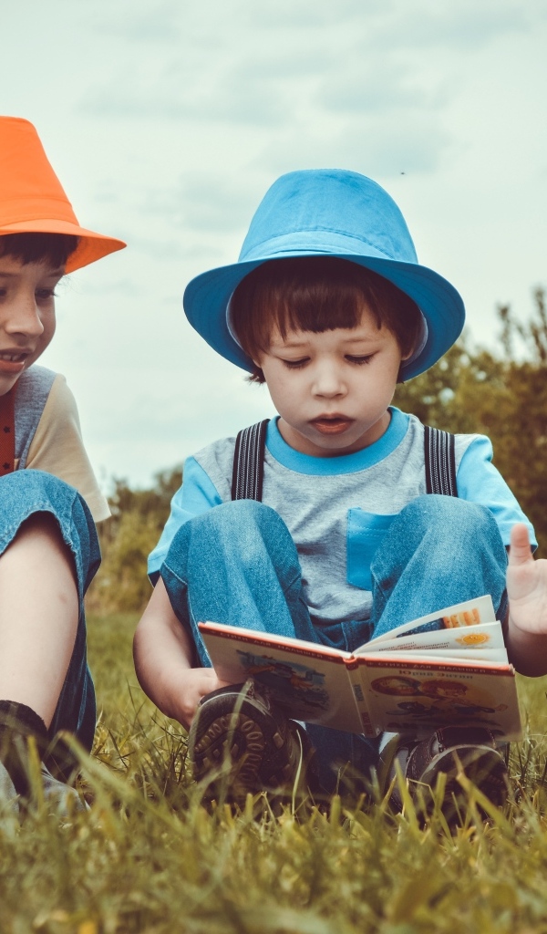 Два маленьких мальчика с книгой сидят на траве