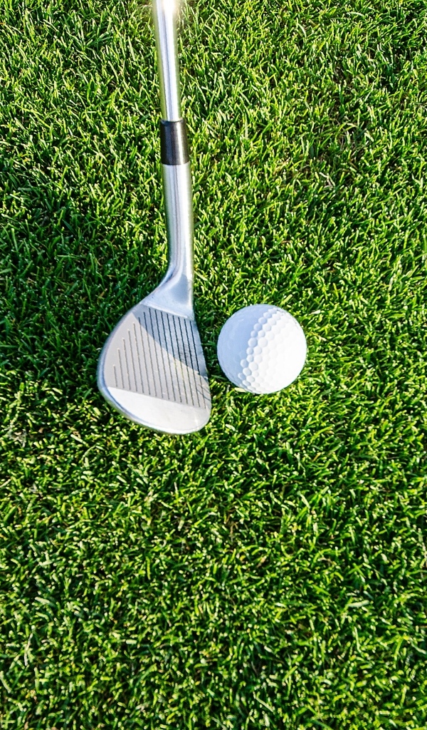 Клюшка и белый мяч для гольфа на зеленой  траве