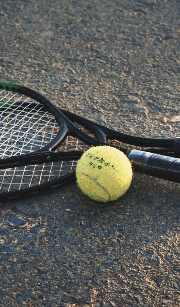Две ракетки и желтый мяч для тенниса на асфальте