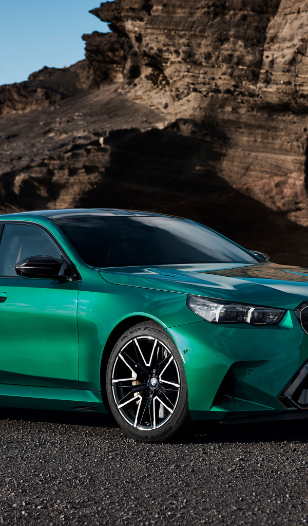 Зеленый автомобиль BMW M5 2024 года на фоне гор