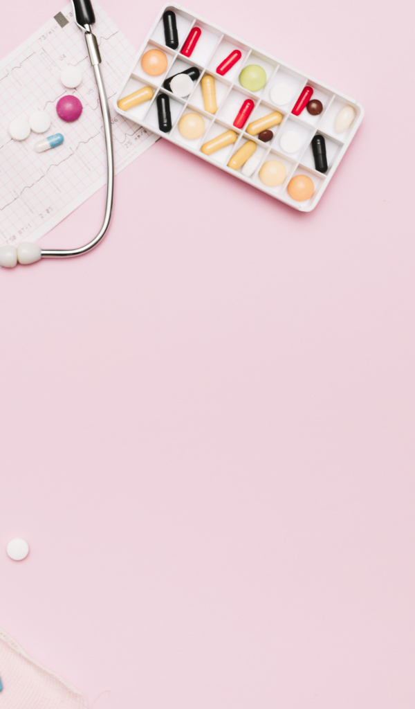 Стетоскоп и лекарства на кардиограмме на розовом фоне