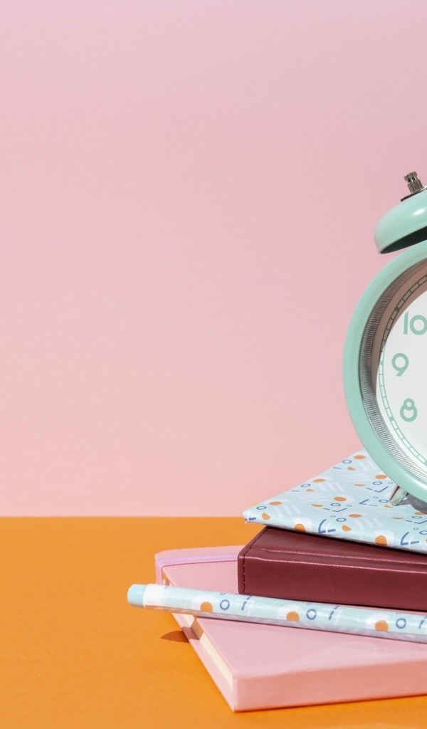 Будильник с книгами на розовом фоне