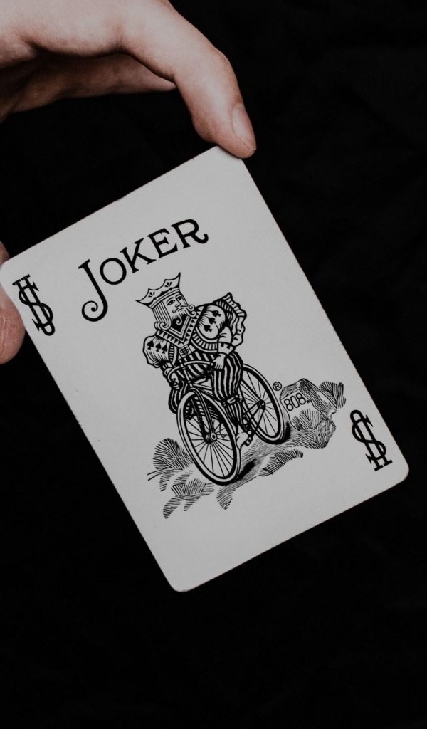 Карта Джокер в руке на черном фоне