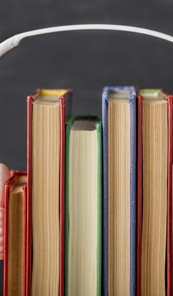 Разноцветные книги с белыми наушниками на сером фоне