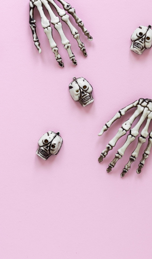 Кисти рук скелета и черепа на розовом фоне