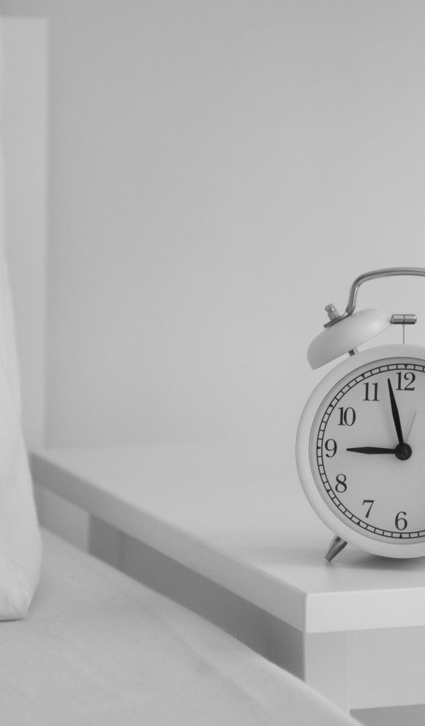 Будильник стоит на тумбочке у кровати 