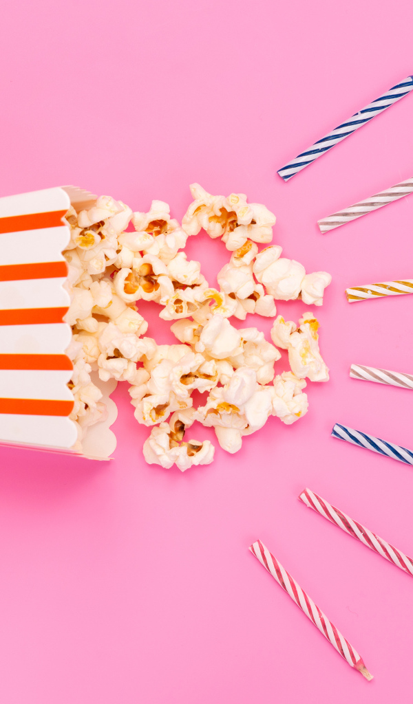 Коробка попкорна со свечами на розовом фоне