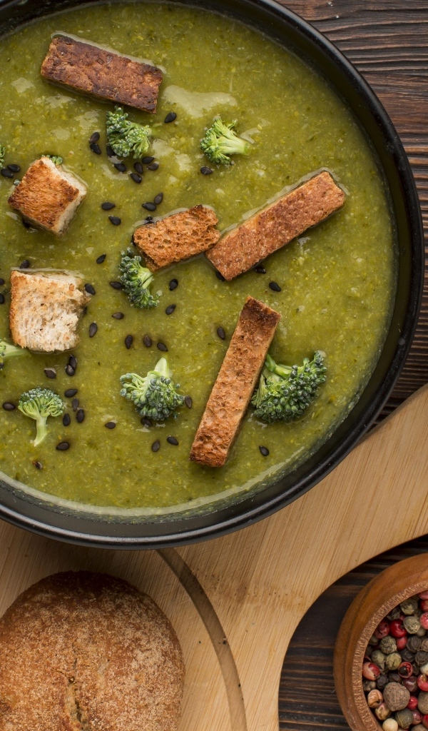 Зеленый суп пюре на столе с сухариками и перцем