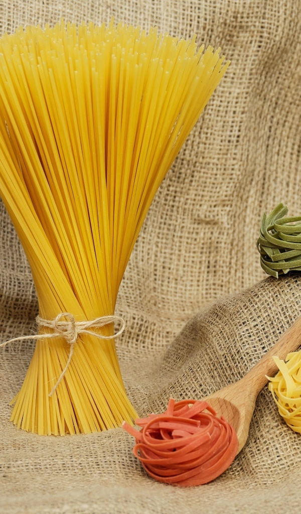 Разноцветные макаронные изделия с деревянной ложкой на мешке