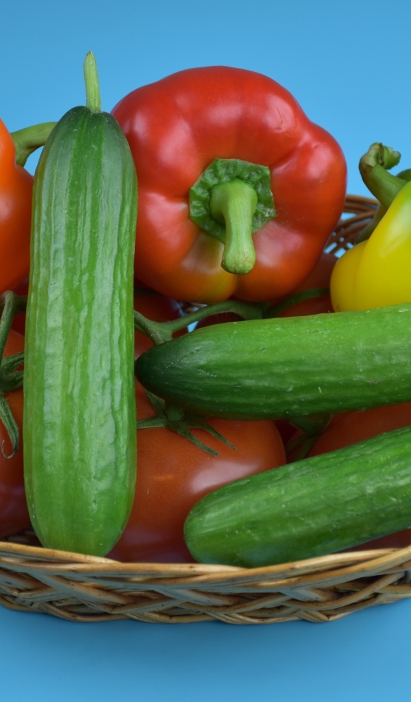 Перец, помидоры и огурцы в корзине на голубом фоне