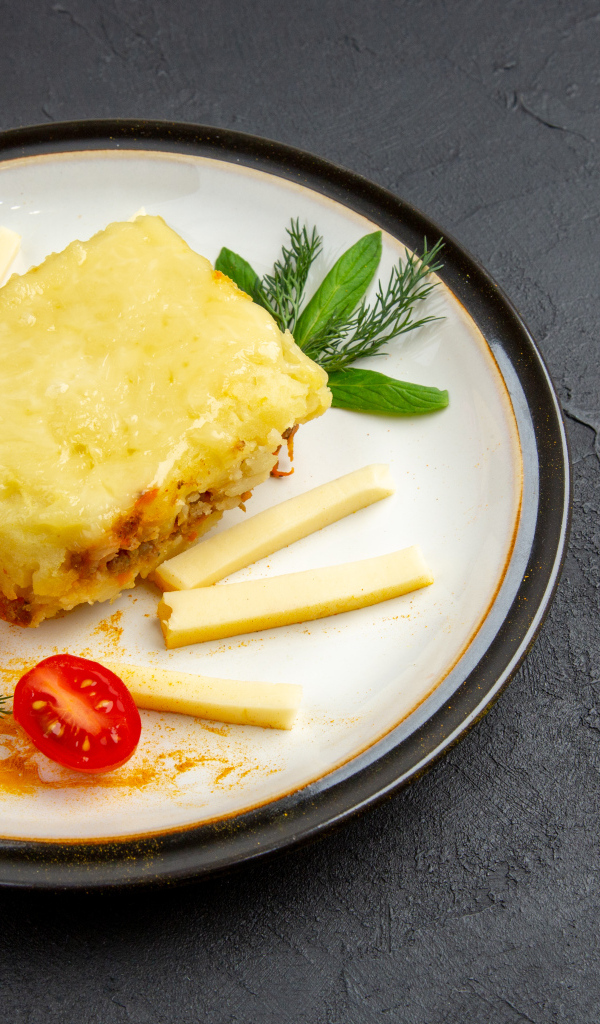 Кусок картофельной запеканки на тарелке с помидорами