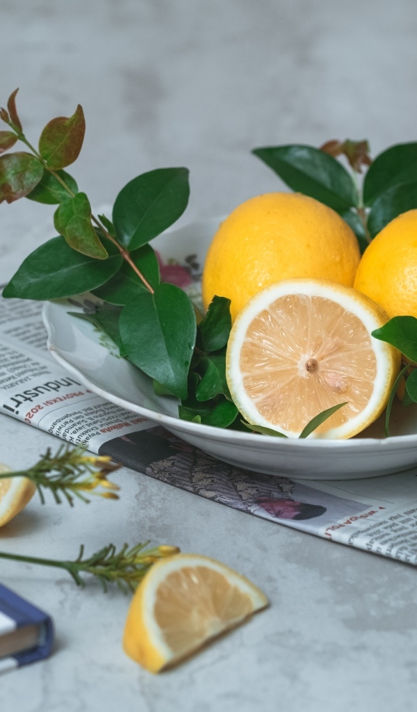 Лимоны на тарелке с зелеными листьями