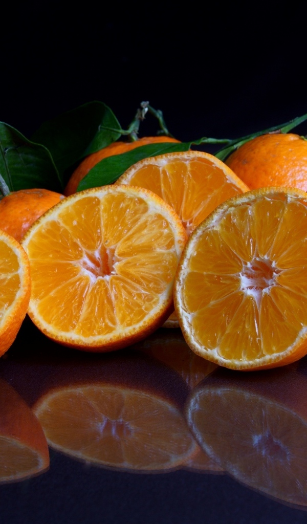 Половинки мандарина с листьями на черной поверхности