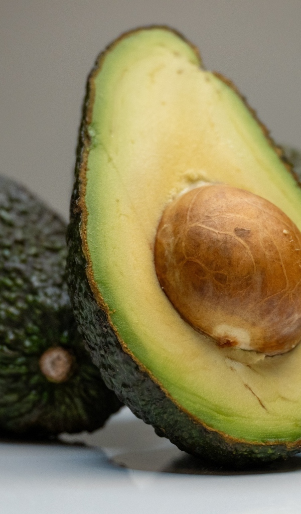 Спелое зеленое авокадо с косточкой на сером фоне