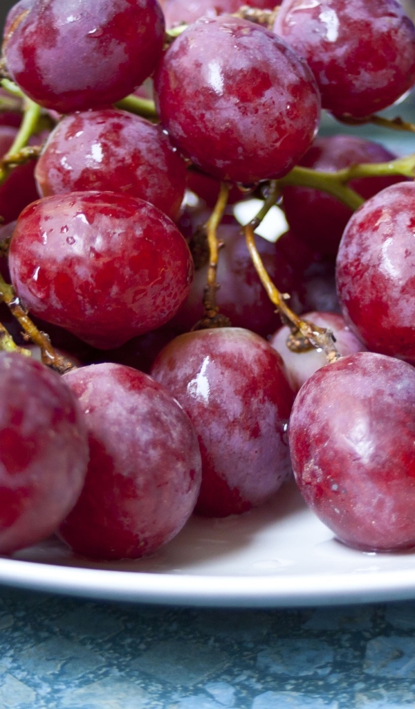 Спелый розовый виноград на белой тарелке