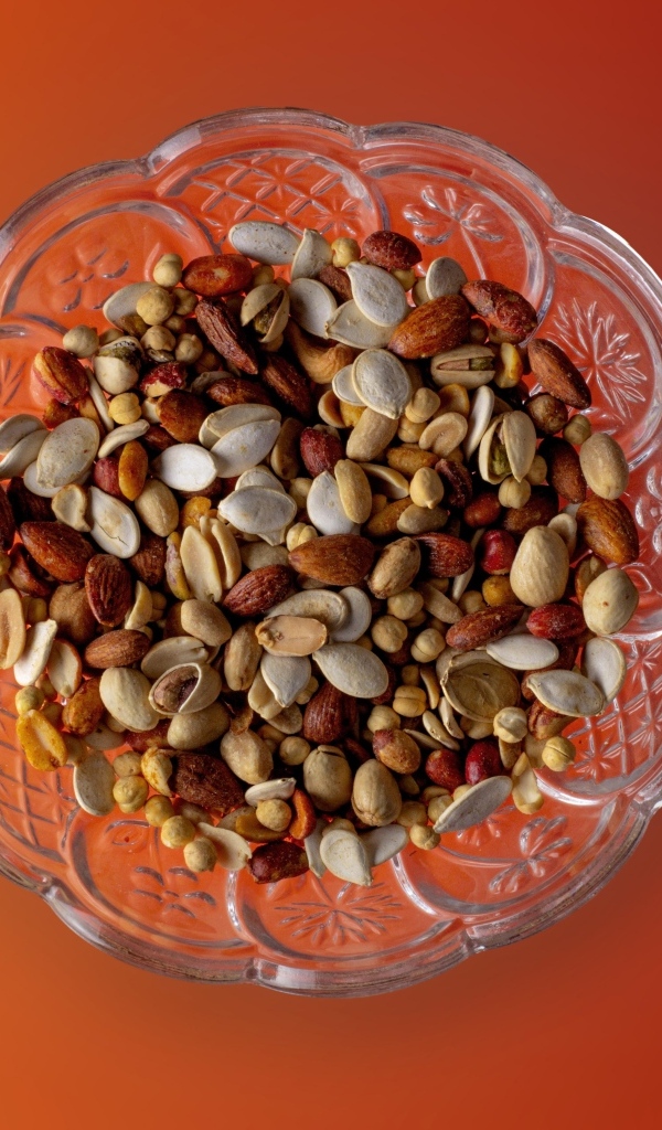 Семечки и орехи в стеклянной вазе на оранжевом фоне