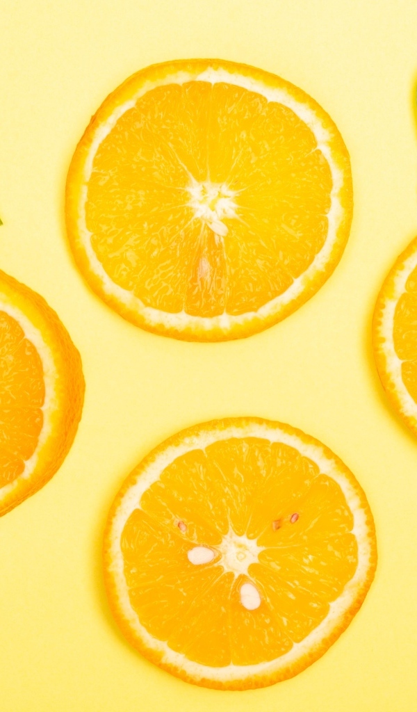 Нарезанный апельсин с зелеными листьями на желтом фоне