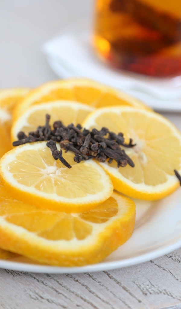 Нарезанный апельсин и лимон на тарелке с гвоздикой