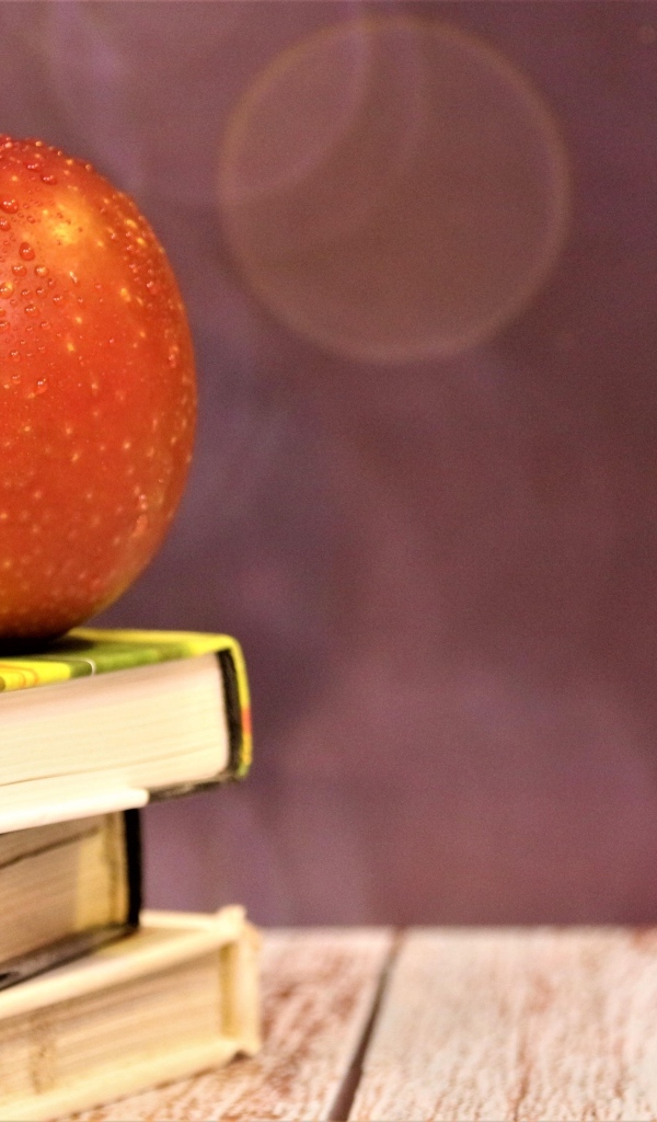 Мокрое яблоко на столе с книгами