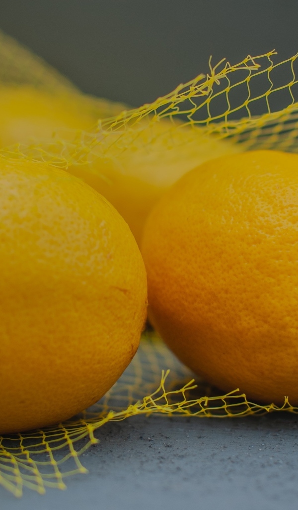 Желтые лимоны в сетке на сером столе