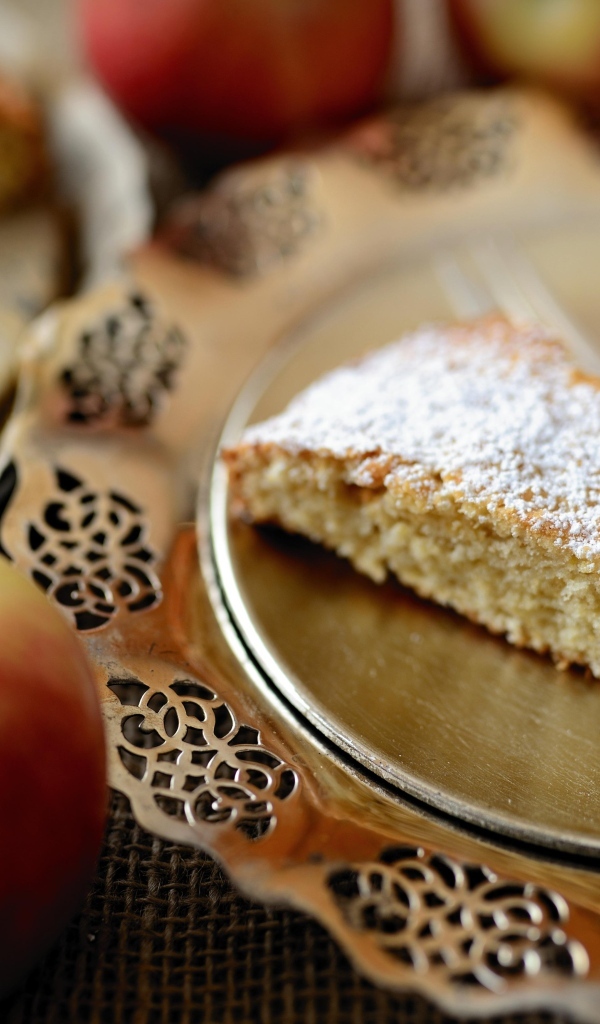 Кусок пирога с сахарной пудрой на столе с яблоками