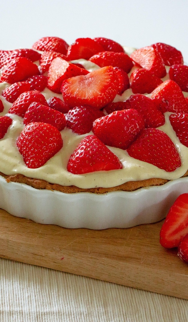 Большой пирог с кремом и ягодами спелой клубники на столе