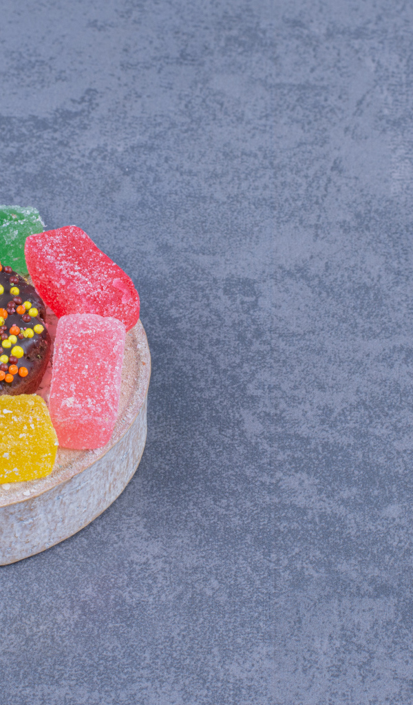 Разноцветные мармеладные конфеты и пончик на сером столе