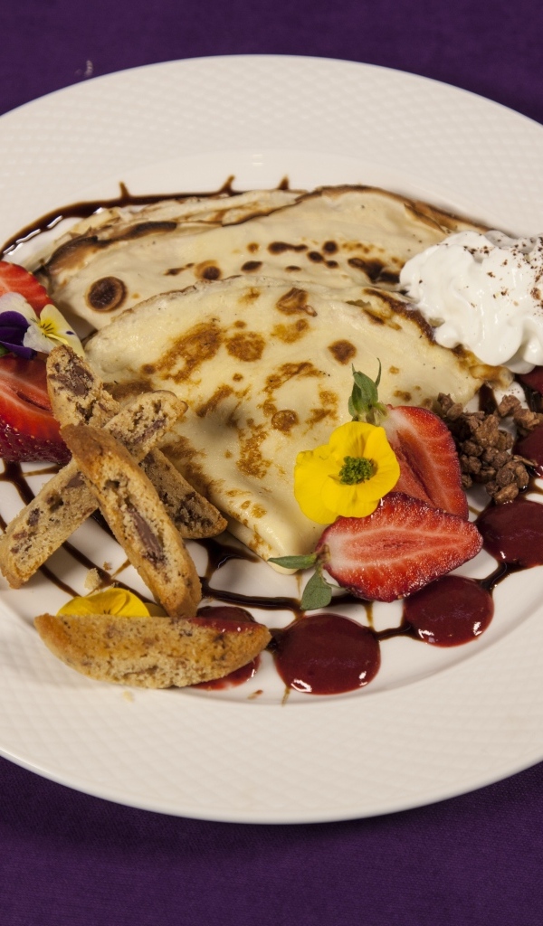 Тонкие блинчики с кремом и ягодами на тарелке