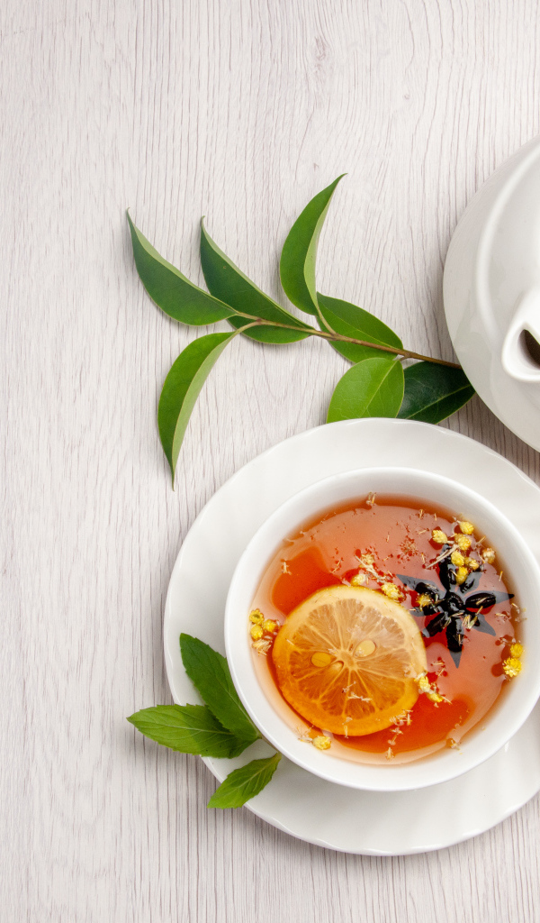 Вкусный чай в белой чашке на столе с лимоном и чайником