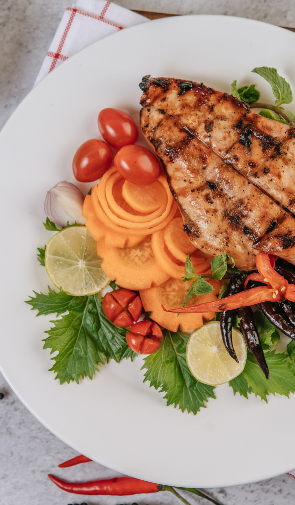 Кусок жареной курицы на большой белой тарелке с овощами