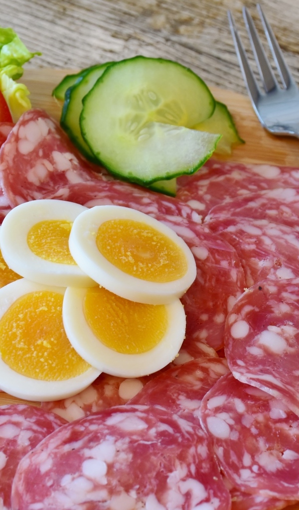 Колбаса салями на доске с вареными яйцами и овощами