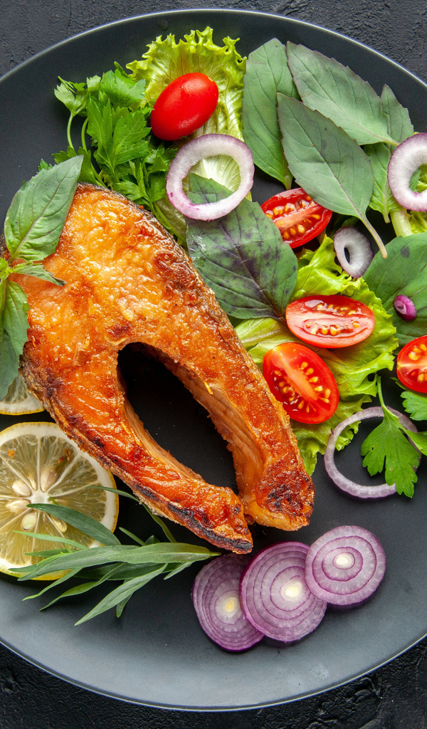 Жареная рыба на тарелке с зеленью,  лимоном и помидорами