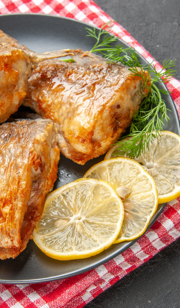 Куски жареной рыбы на тарелке с кусочками лимона и укропом