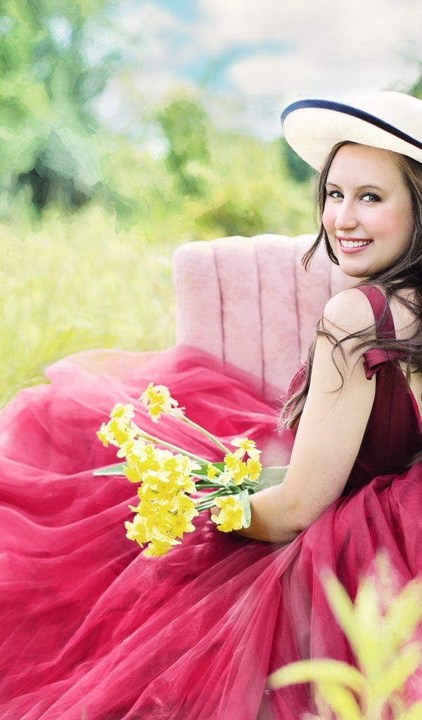 Красивая девушка в розовом платье сидит на кресле в траве