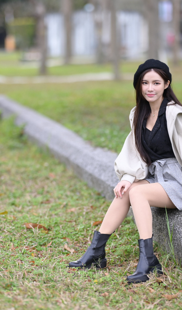 Девушка в пальто сидит на земле в парке