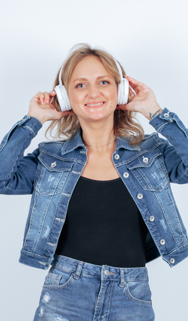 Девушка в джинсовом костюме с наушниками на голове на фоне стены