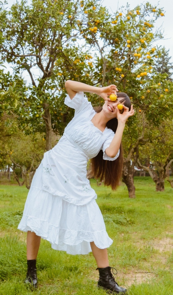 Девушка в белом платье закрыла глаза лимонами