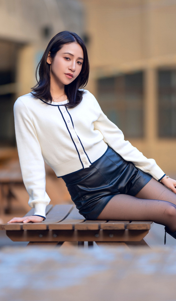 Азиатка в черных кожаных сапогах лежит на деревянном столе