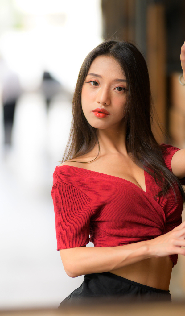 Азиатка в красном топе стоит у стены