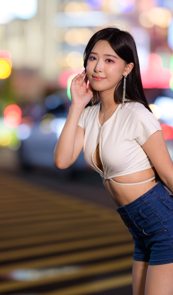 Азиатка в коротких шортах стоит на дороге в городе