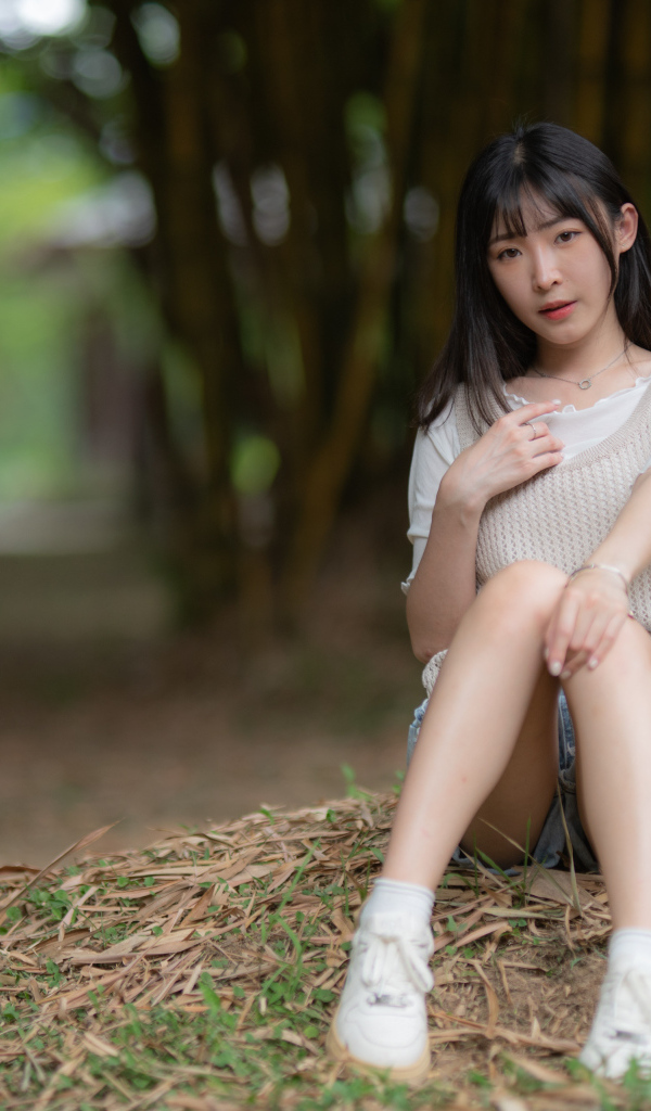 Азиатка сидит на земле в парке