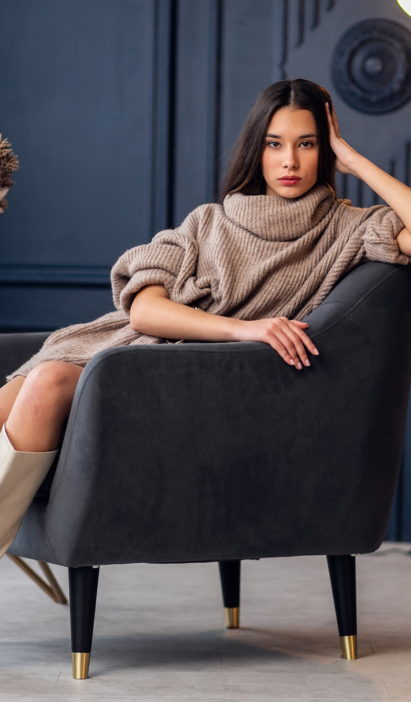 Красивая брюнетка в сапогах сидит в кресле