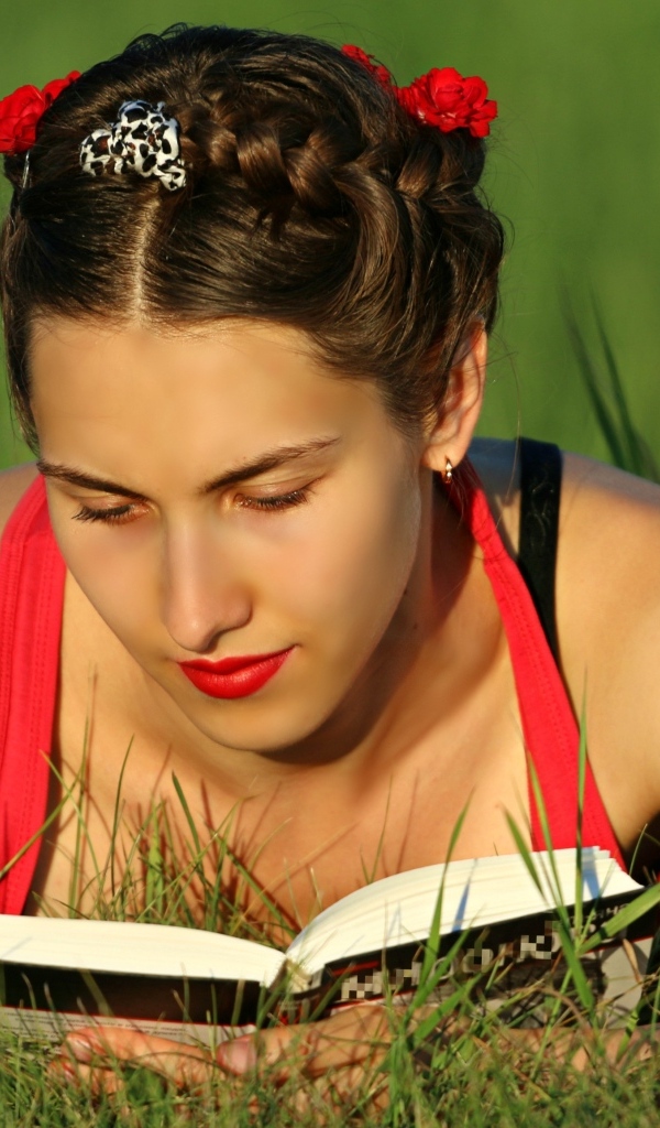 Красивая девушка читает книгу лежа на траве