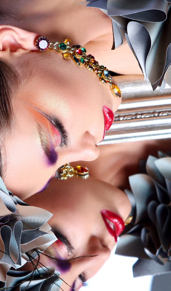 Красивая девушка с ярким макияжем отражается в зеркале